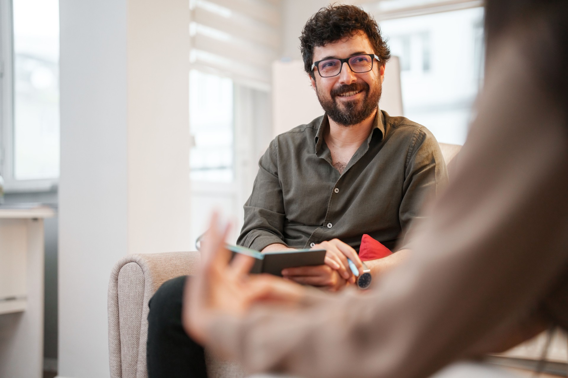 The psychologist who is listening to the patient is taking notes in his notebook